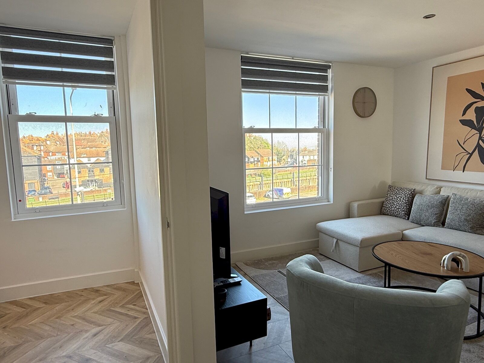 A living room with two large windows, a sofa, a coffee table, and a television.