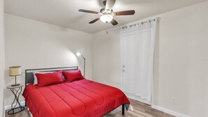A bedroom with a bed, a ceiling fan, a nightstand, a lamp, and a white door.