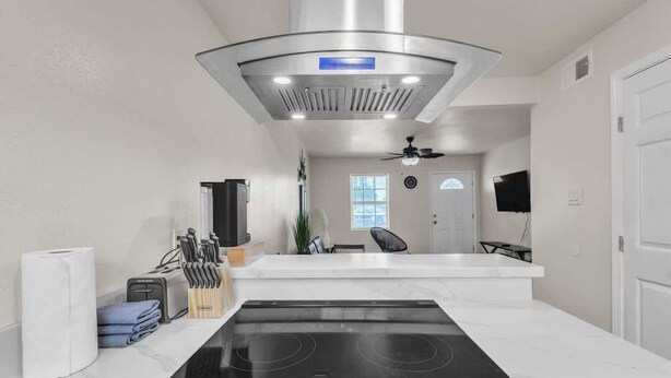 A modern kitchen with a black stovetop, white countertops, and a stainless steel range hood.