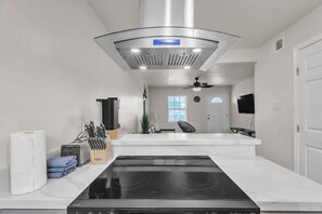 Eine moderne Küche mit einer schwarzen Kochplatte, weißen Arbeitsflächen und einer Edelstahl-Dunstabzugshaube.