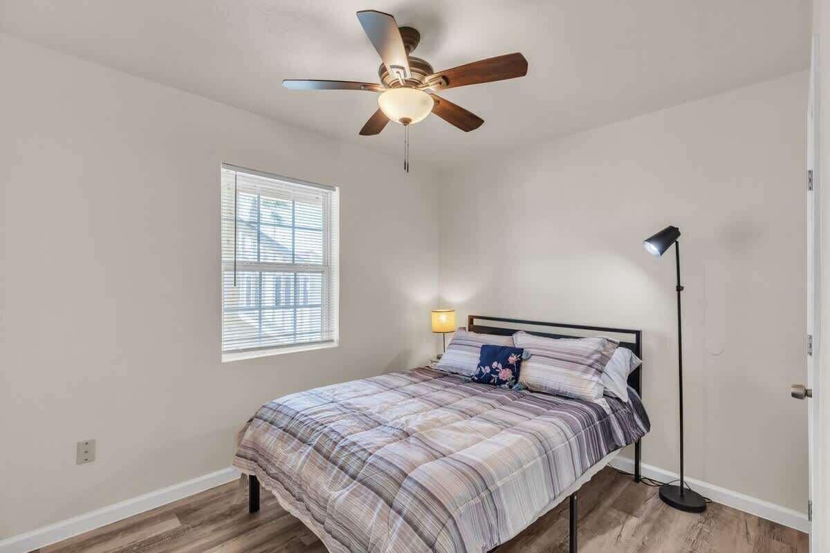 Ein Schlafzimmer mit einem Bett, einem Deckenventilator, einer Stehlampe und einem Fenster mit Jalousien.
