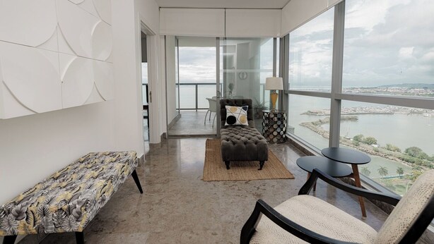 Ein geräumiges Zimmer mit großem Fenster, einer Couch, einem kleinen Tisch und einer Bank.