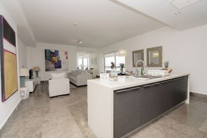 Una cucina moderna con isola centrale, una zona pranzo con tavolo e sedie bianche e un soggiorno con divano e tavolino.