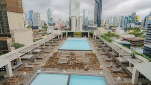Ein Poolbereich auf dem Dach mit mehreren Pools, Liegestühlen und Blick auf die Stadt.