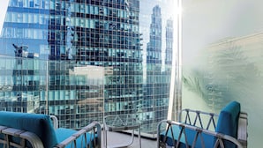 Une chambre d’hôtel moderne avec une cloison en verre, deux fauteuils bleus et un petit guéridon en verre.