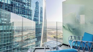 Un immeuble de grande hauteur avec une façade en verre, un balcon agrémenté d’un canapé bleu et d’une petite table, et une vue sur le paysage urbain.