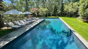 Ein rechteckiger Swimmingpool mit klarem, blauem Wasser, umgeben von einer gepflegten Rasenfläche und Bäumen.