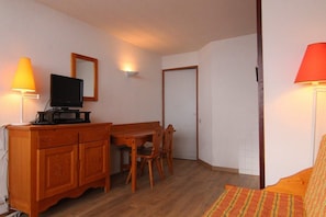 A small, cozy room with a wooden dining table and chairs, a television on a cabinet, and two lamps.