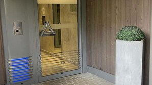 A modern elevator with a metallic finish, a glass door, and a control panel on the left.