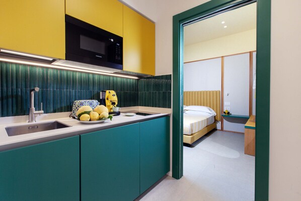 A compact kitchen with a sink, a microwave, and a countertop with fruits and a teapot. - Casa Pina Emerald (Sorrento)