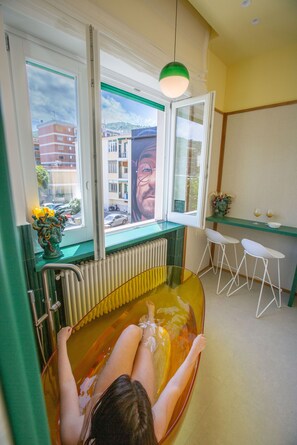 A bathtub with a view of buildings outside, a radiator, a green wall, and a window with an open shutter. - Casa Pina Emerald (Sorrento)