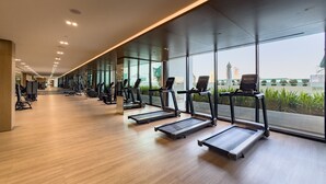 A modern gym with treadmills aligned along a wall with large windows, providing views of a cityscape.