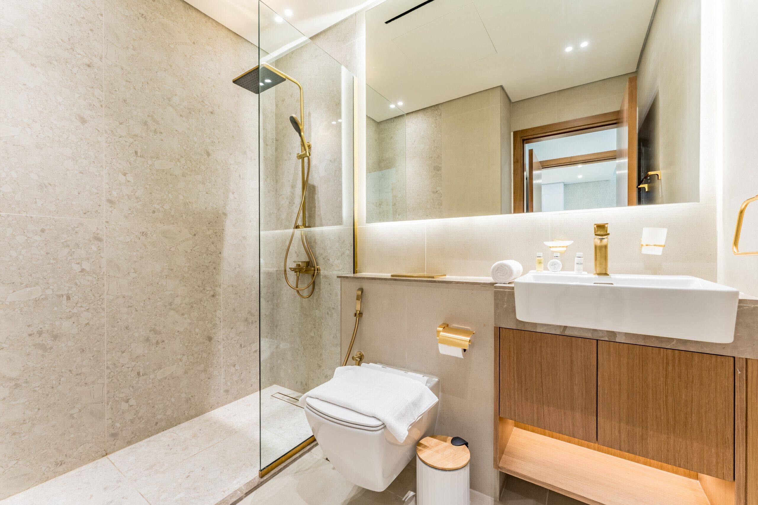 A modern bathroom with a glass-enclosed shower, a white toilet, a wooden vanity, and a large mirror.