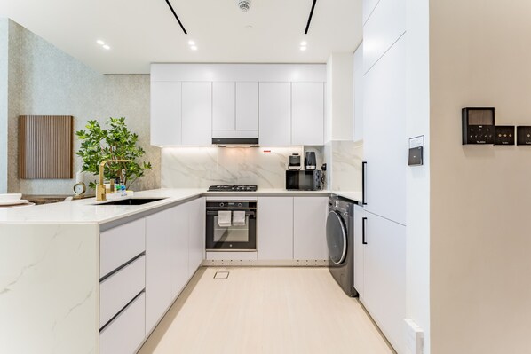 A modern kitchen with white cabinets, a built-in oven, a washing machine, and a coffee machine.