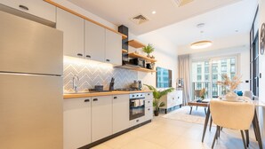 Une cuisine moderne dotée d’appareils électroménagers intégrés, un coin repas avec une table et des chaises, et une grande fenêtre qui laisse entrer la lumière naturelle.