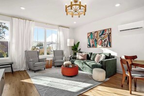 Uma sala de estar moderna com um sofá verde, duas poltronas, um banquinho vermelho e uma mesa de jantar com cadeiras.