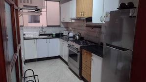 Une cuisine de taille r éduite avec des meubles blancs, un réfrigérateur en acier inoxydable, une cuisinière et un évier.