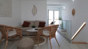 Ein Wohnzimmer mit einer Couch, zwei Korbstühlen, einem kleinen Tisch und einer Topfpflanze.