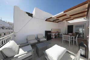Une terrasse sur le toit, avec des meubles blancs, un barbecue et un espace repas.