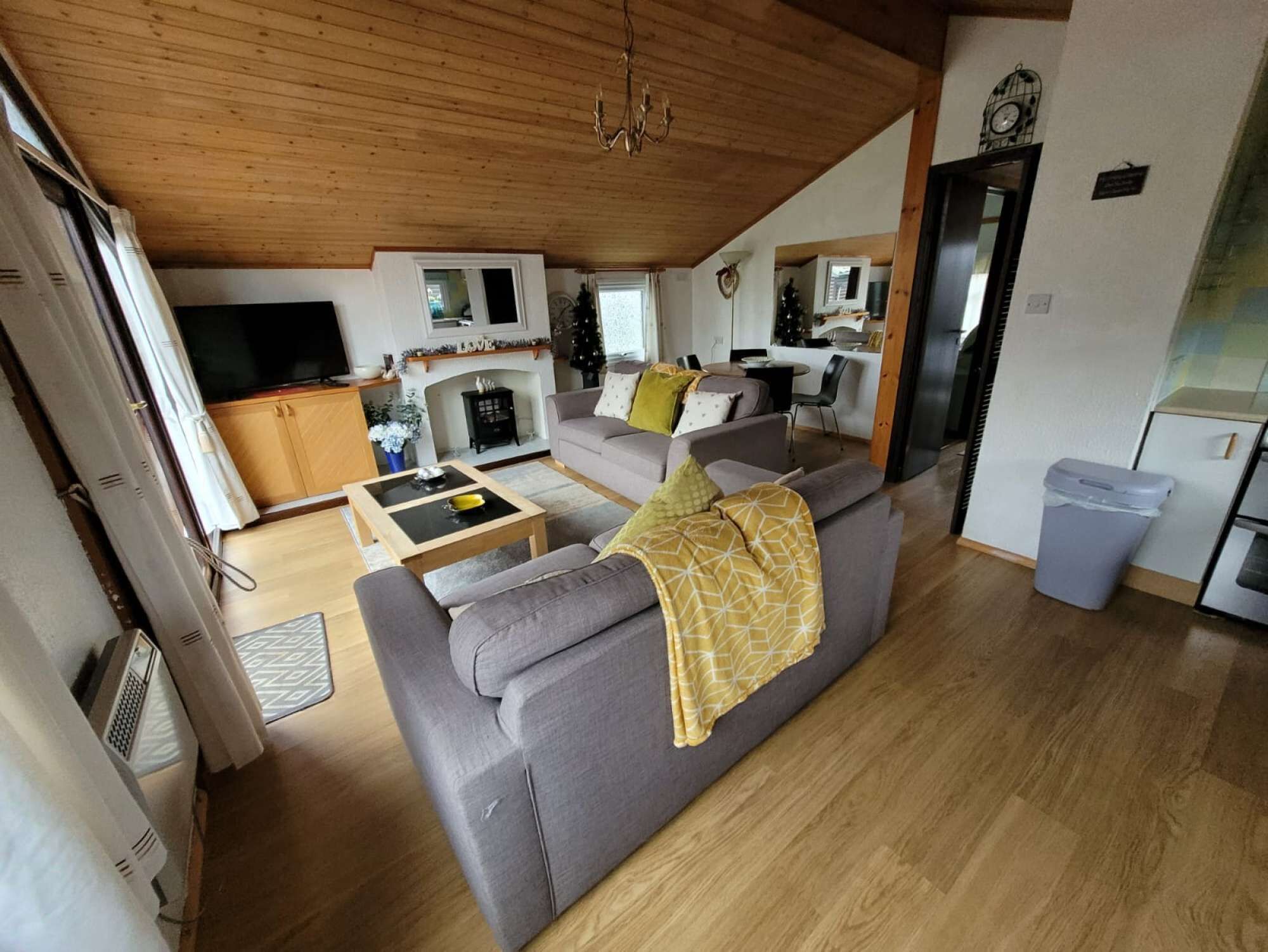 Amplia sala de estar con sofá, mesa de centro y chimenea. Se observa una cocina con refrigerador y mesa de comedor.