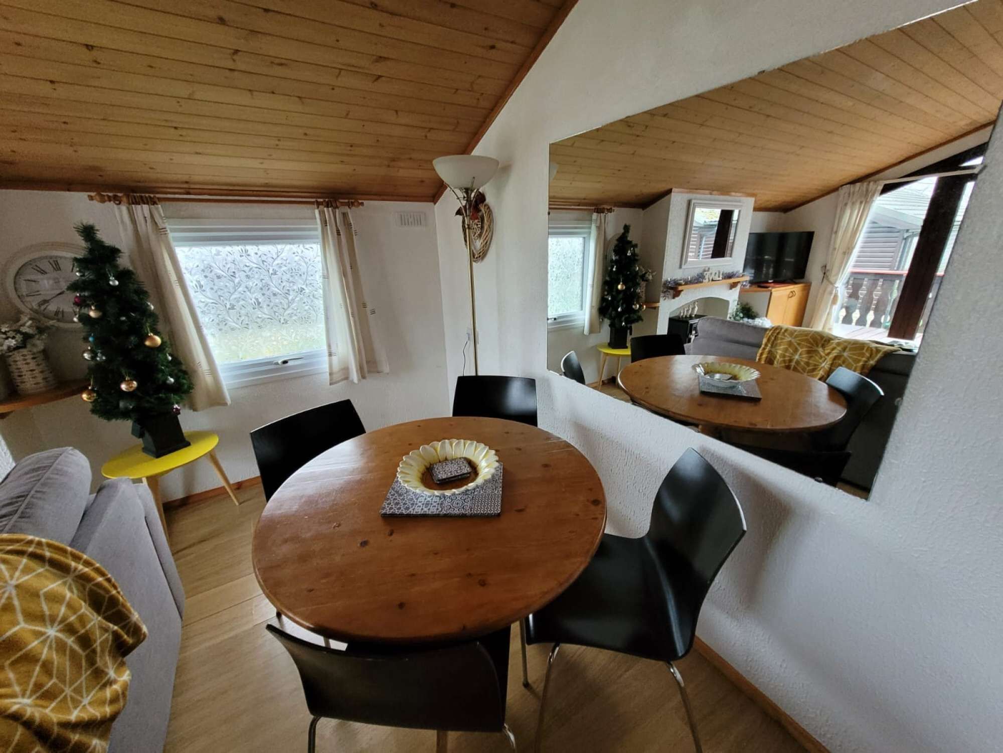 A cozy dining area with a wooden table and black chairs, a Christmas tree, and a view of a kitchen and living area.