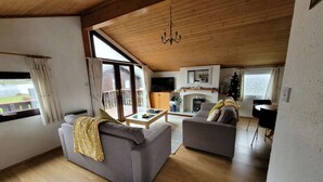 A spacious living room with a high ceiling, a fireplace, a television, and a cozy seating area. - Bumble Bee Cabin on Heron Lake (Hoburne Holiday Park)