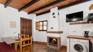 Cuina amb llar de foc, rentadora, televisió i zona de menjador amb cadires i taula.