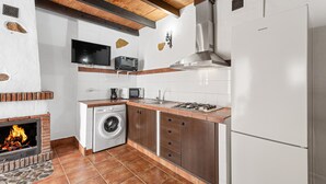 Cuina amb una llar de pedra, rentadora, microones i nevera.