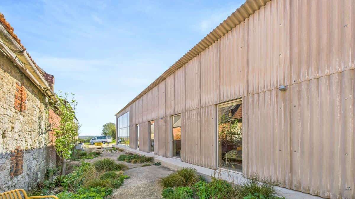 A modern building with a corrugated metal exterior, a paved pathway, and a small garden area.