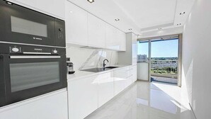 Eine moderne Küche mit Backofen von Bosch, weißen Schränken, einer Spüle aus Edelstahl und einem großen Fenster mit Blick auf die Stadt.