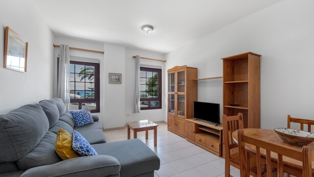Una sala de estar con un sofá gris, un mueble de televisión de madera y una mesa de comedor con sillas.