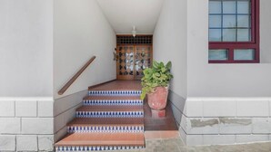 Una escalera conduce a una puerta con piso de baldosas estampadas y una planta en maceta.