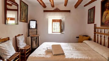 A room with a bed, wooden chairs, a small table, and a window.