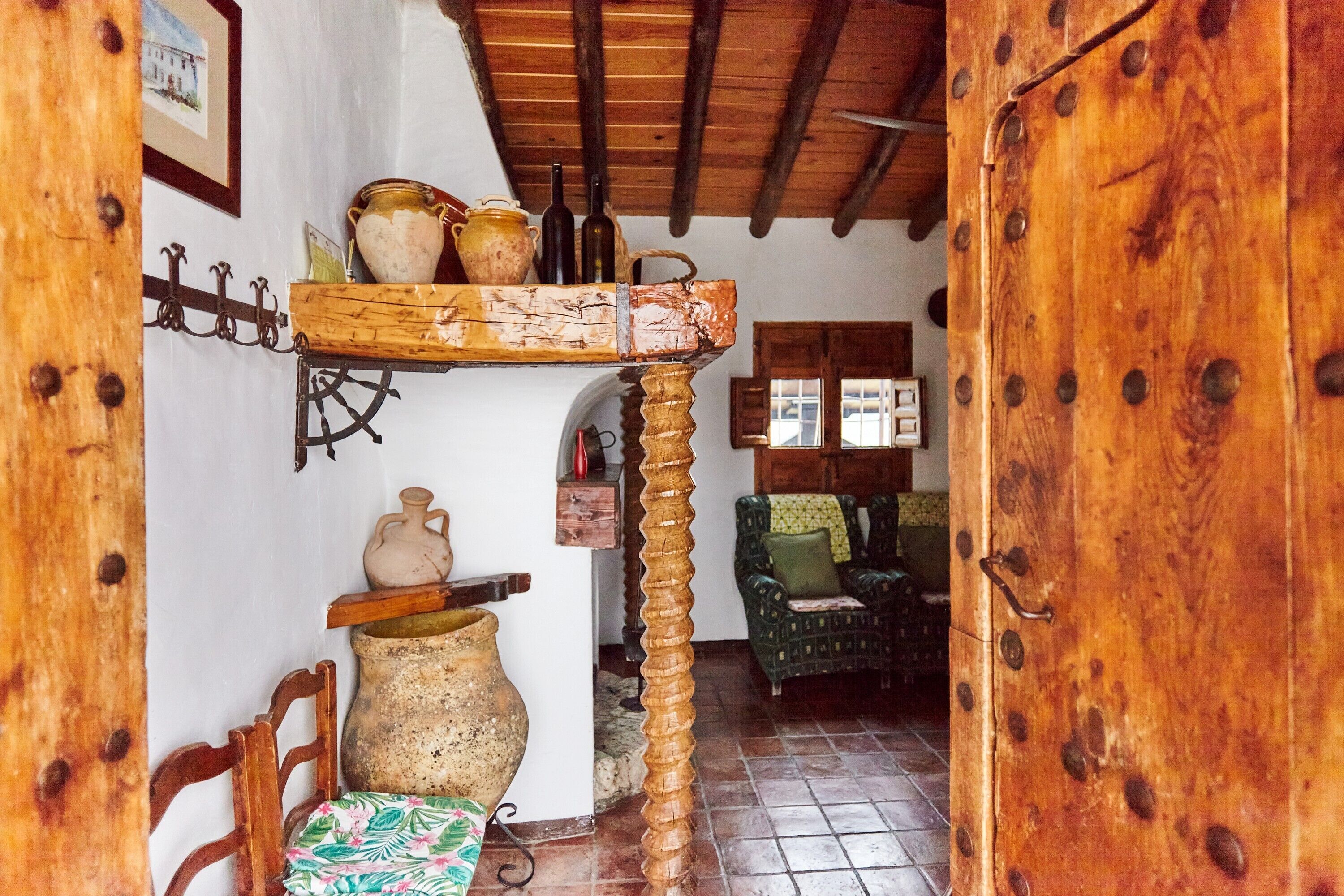 Un interior rústico con una puerta de madera, un estante con cerámica y una silla.