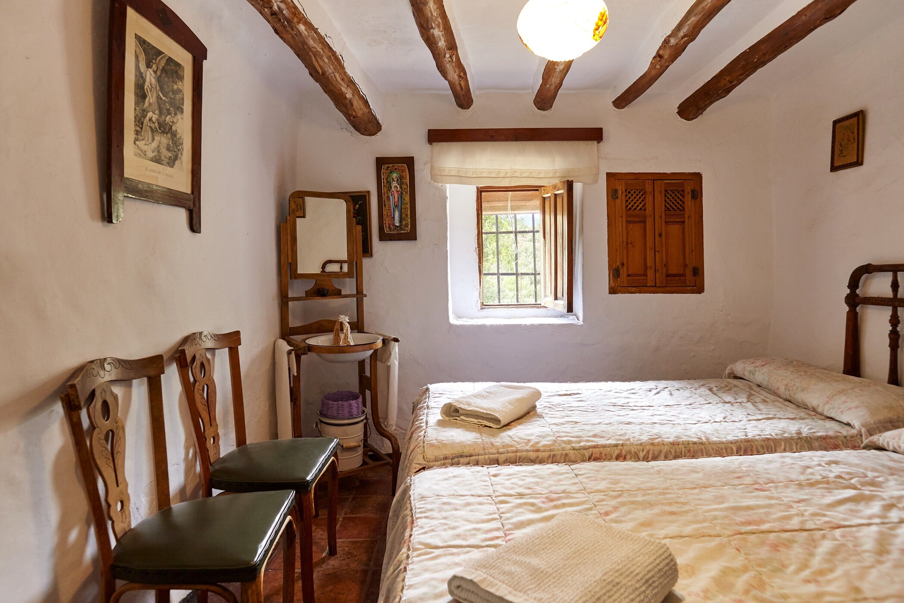 Ein Schlafzimmer mit zwei Betten, einem Holzsessel, einem kleinen Tisch und einem Fenster mit Blick.