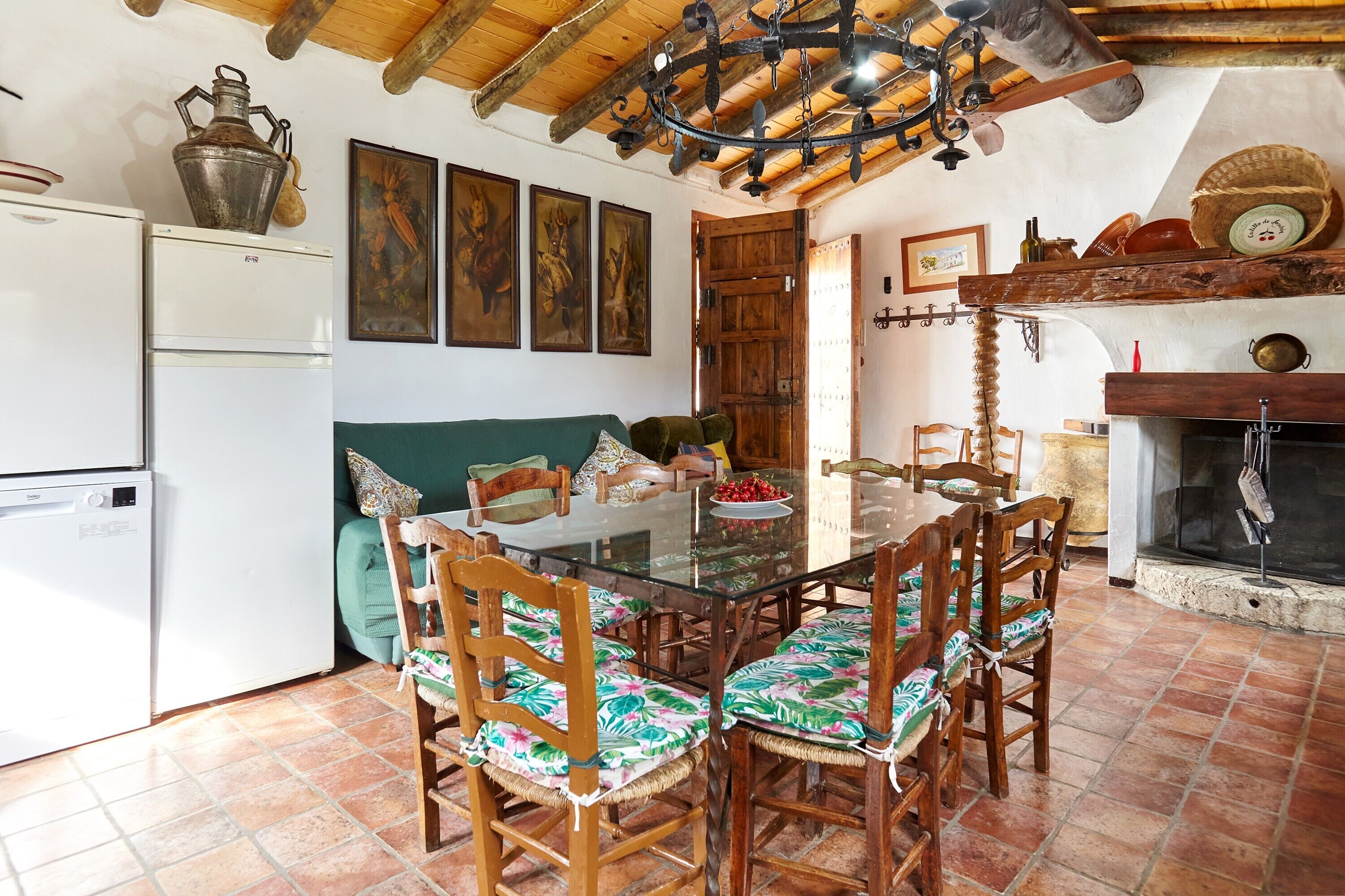 Zona pranzo con tavolo in vetro, sedie in legno, divano verde e camino.