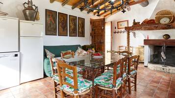 Zona pranzo con tavolo in vetro, sedie in legno, divano verde e camino.