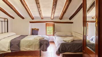 Quarto com duas camas, vigas de madeira no teto, janela e porta com espelho.
