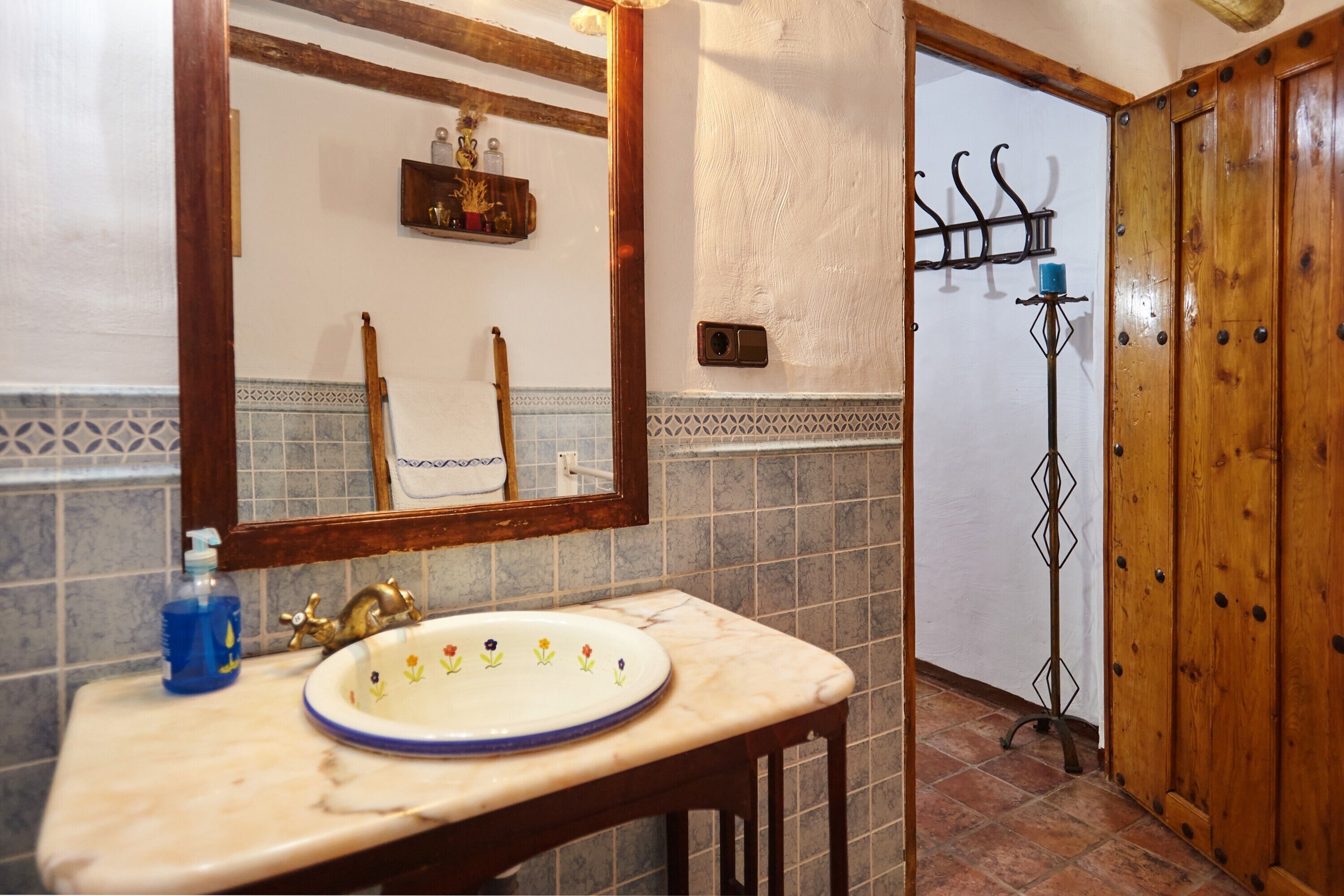 Un baño con lavamanos de mármol, tocador de madera, espejo y zona de ducha con puerta de madera.