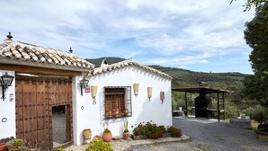 A rustic building with a tiled roof, a wooden door, and a small window. There are potted plants and a barbecue grill in the foreground. - Cottage 'Majolero 2' with Shared Pool, Wi-Fi and Air Conditioning (Castillo de Locubín)