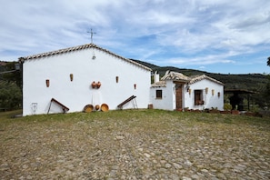 Un edificio blanco con una cruz en el techo, un pequeño ala y suelo adoquinado.