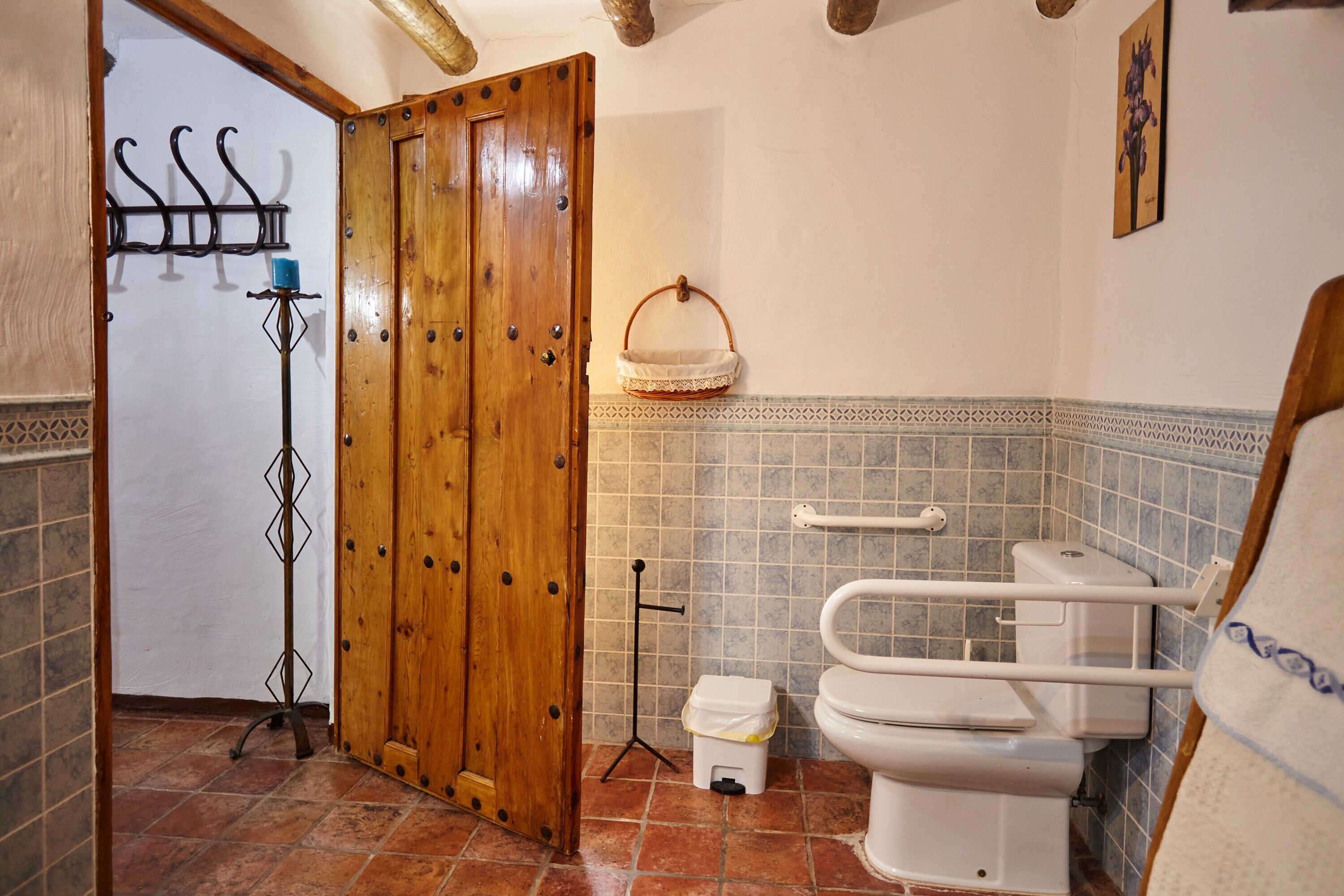 A bathroom with a wooden door, a white toilet, a grab bar, and a tiled floor.