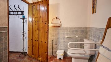 A bathroom with a wooden door, a white toilet, a grab bar, and a tiled floor.