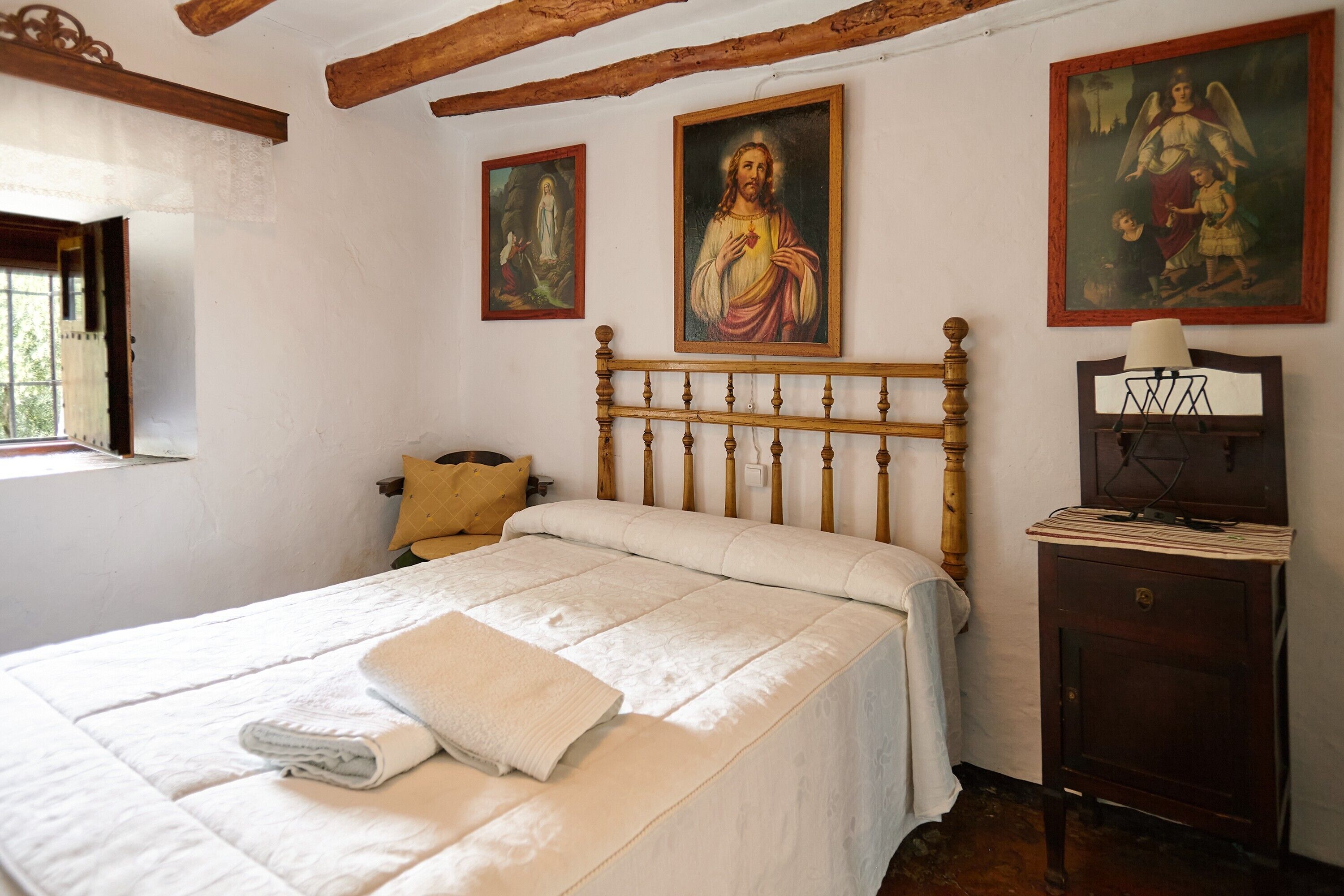 Un dormitorio con una cama de madera, una mesita de noche y tres cuadros religiosos en la pared.