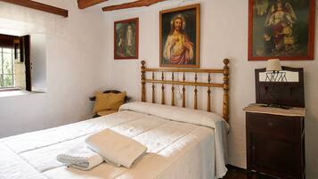 Un dormitorio con una cama de madera, una mesita de noche y tres cuadros religiosos en la pared.