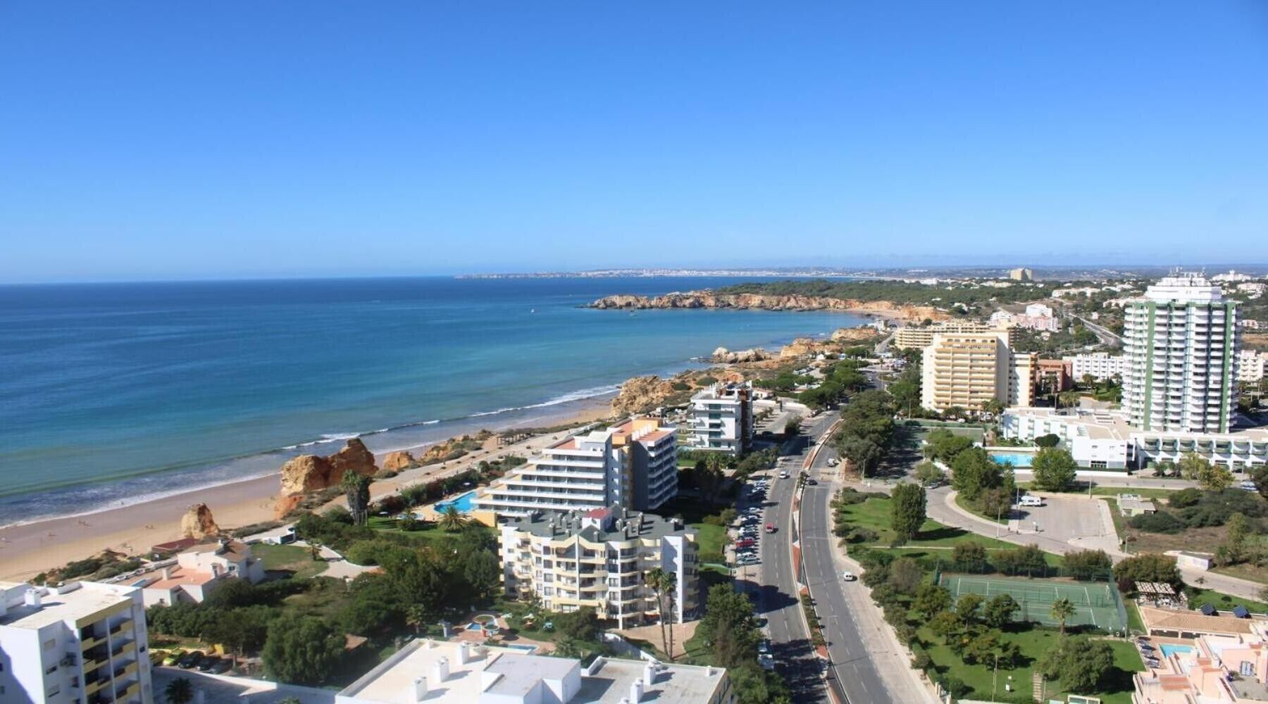 Paisagem costeira urbana com praia, edifícios altos e céu azul límpido.