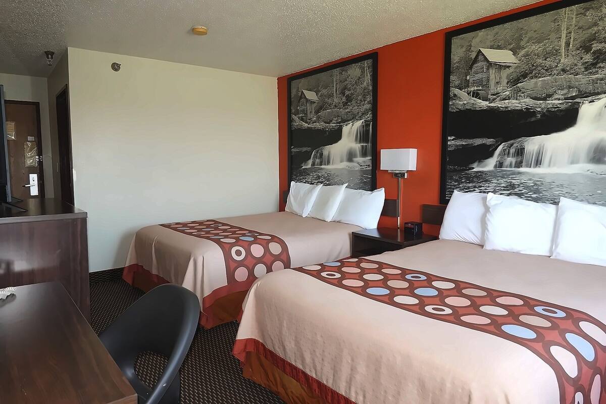 A hotel room with two beds, a desk, a chair, and a large wall-mounted picture of a waterfall.