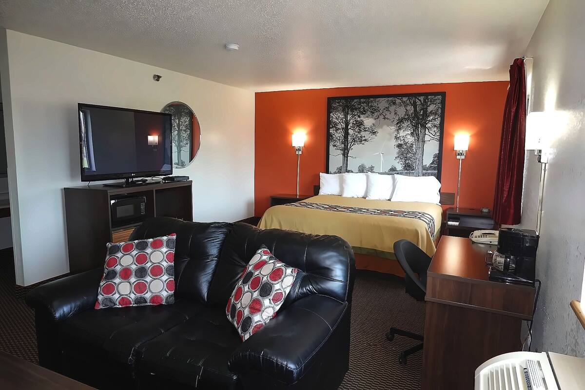 A hotel room with a bed, a black leather sofa, a TV, and a desk with a coffee maker.