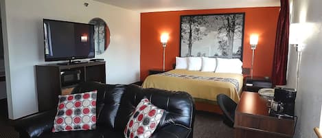 Una habitación de hotel con una cama, un sofá de cuero negro, un televisor y un escritorio con cafetera.