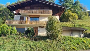 Eine zweistöckige Chalet mit Balkon, umgeben von üppiger Vegetation und Bäumen.